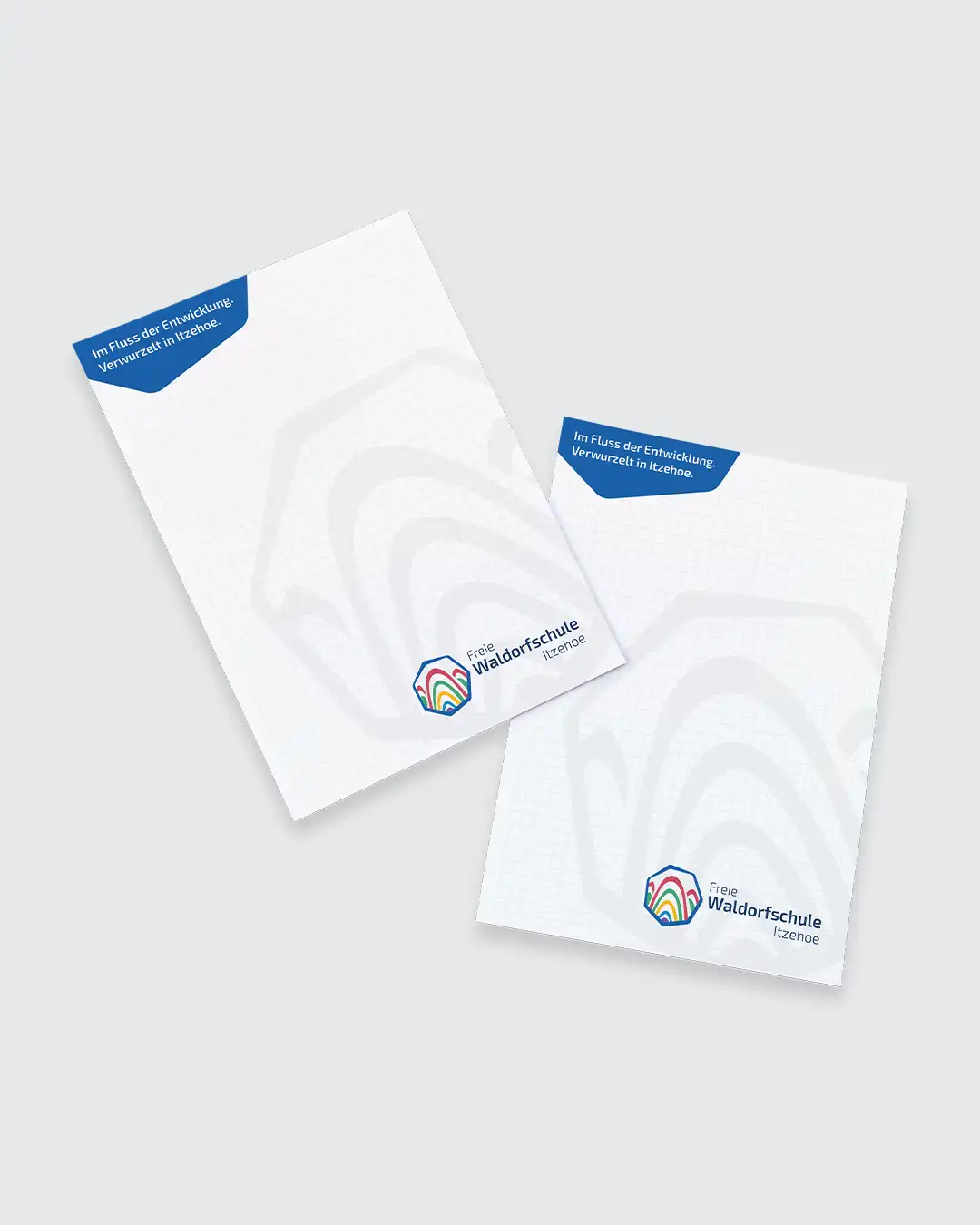 Mockup zweier Schreibblöcke im neuen Corporate Design der Freien Waldorfschule Itzehoe mit Schullogo, Slogan und dezentem grafischem Wasserzeichen.